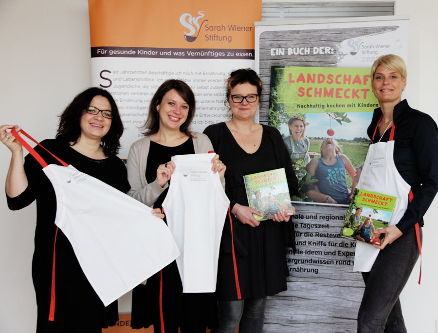 Diana Beyer und Anja Dümichen (beide PROMOS) bei der Übergabe von Kochschürzen für die Sarah-Wiener-Stiftung in Berlin PROMOS unterstützt Sarah-Wiener-Stiftung
